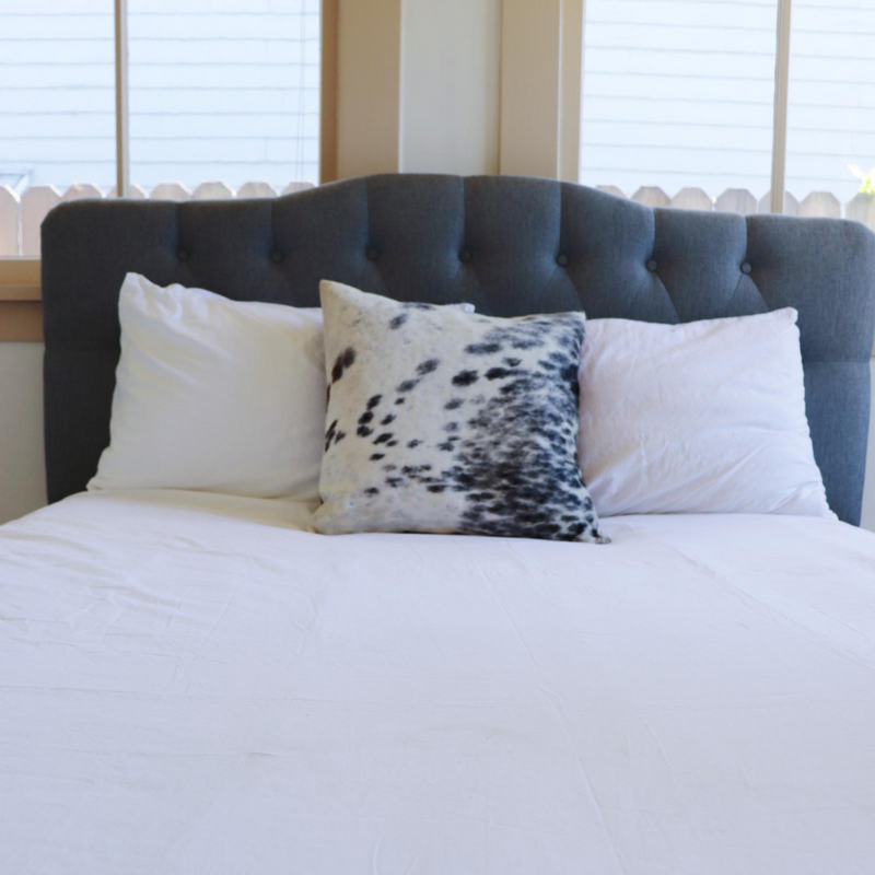 A handmade cowhide pillow in white and black spots decorating a bed