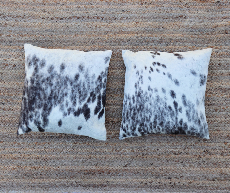 Two white and black spot cowhide RoHo  accent pillows from Kenya laying side by side
