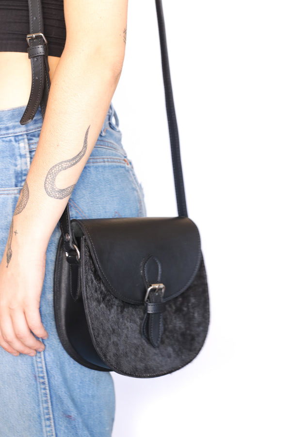 RoHo's artisan made Kenyan cowhide crossbody saddle purse in black hide and black finished leather on a model