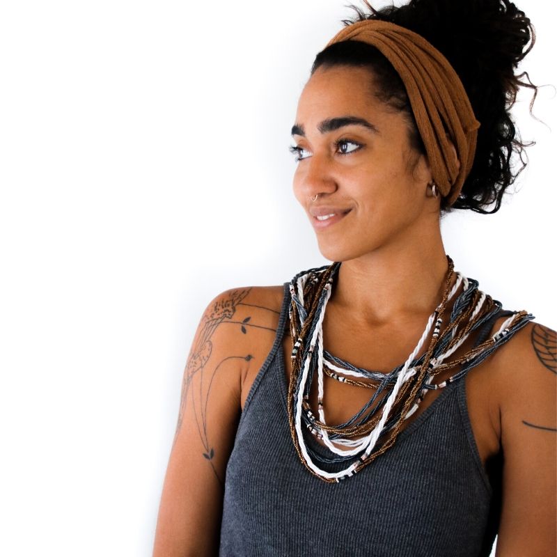 Several pieces of Fair Trade Kenyan jewelry on a model. Multiple single strand beaded RoHo necklaces in white, gold and metallic silver with accents