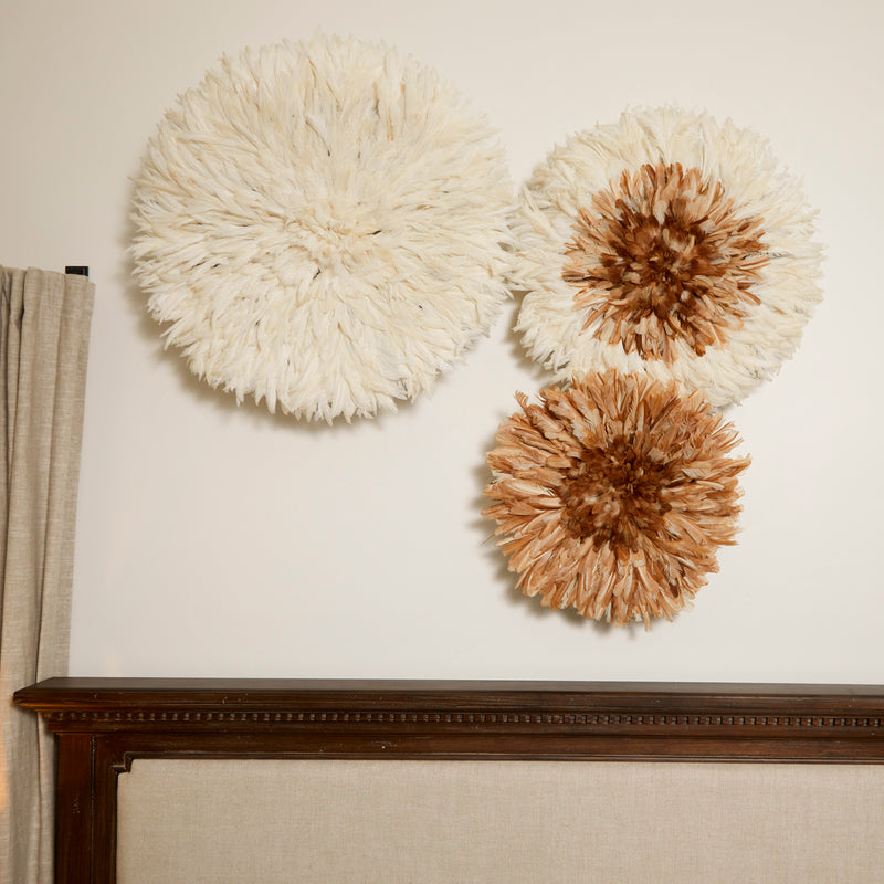 Several RoHo handmade chicken feather Juju hats used as home decor on a wall in tan and white in 18 inches, 24 inches and 30 inches