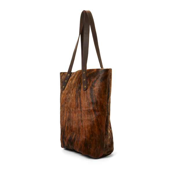 The side of RoHo's Handcrafted Brindle Cowhide Tote Bag Handcrafted in Africa with Leather Straps & Gold Brass Button Accents