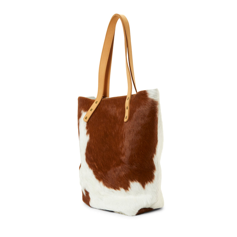 The side of a tan and white cowhide bucket bag by RoHo that gives back