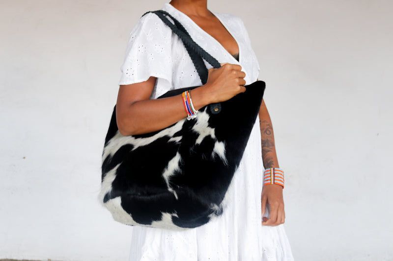 A purposeful RoHo black and white cowhide bucket bag with black handles being worn by a model