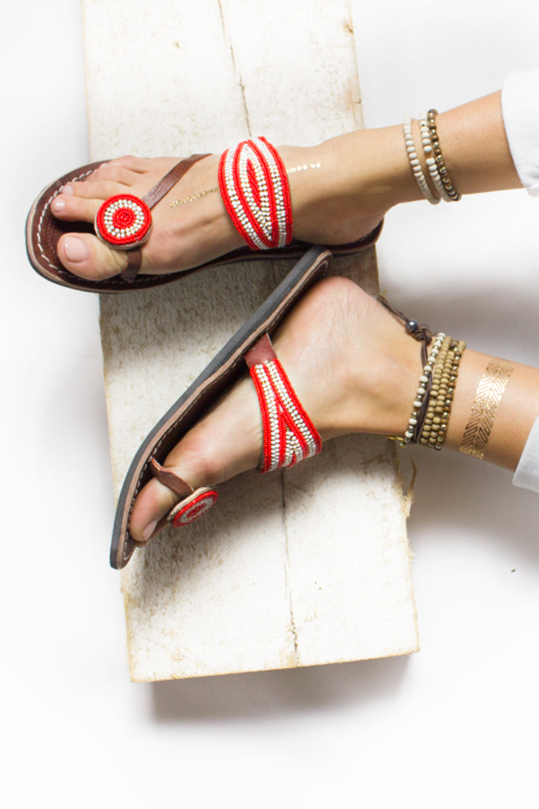 A pair of red and white African beaded leather sandals with a purpose, RoHo's Rafiki sandal, on a model