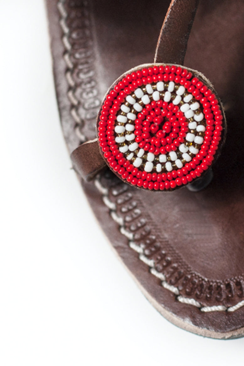 A close up of the bead word on the toe strap of a pair of red and white ethical Kenyan Rafiki Sandals by RoHo